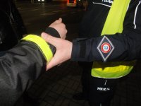 Policjant zakłada opaskę odblaskową pieszemu