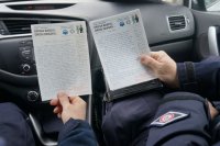 Policjanci siedzą w radiowozie, trzymają w dłoni ulotki