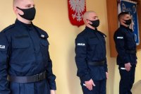 Trzej policjanci stoją w odstępach od siebie, w tle sztandar Komendy Miejskiej Policji w Żorach
