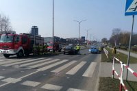 Zdjęcie z miejsca wypadku, na pierwszym planie oznakowane przejście dla pieszych, w tle radiowóz, policjanci, wóż strażacki i strażacy