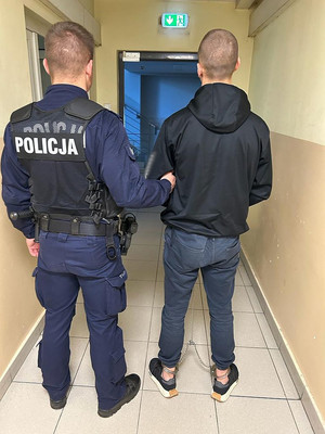 Policjant prowadzi mężczyznę zakutego w kajdanki zespolone