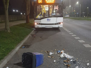 Na zdjęciu widać kosz na śmieci leżący na jezdni, na tle autonbusu