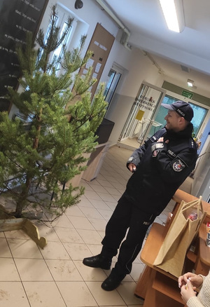 Na zdjęciu widać policjanta, który stoi przed choinką w pomieszczeniach ośrodka interwencji kryzysowej