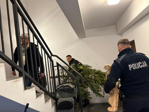 Na zdjęciu widaćstrażaka, pracownika MOPS i dzielnicowego podczas akcji Choinka dla najuboższych, wchodzących po schodach z przygotowanymi prezentami