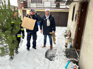 Na zdjęciu widaćstrażaka, pracownika MOPS i dzielnicowego podczas akcji Choinka dla najuboższych, stoją przed jednym z odwiedzanych domów