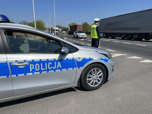 Na zdjęciu widać drogę, przy której stoi policjant. Na pierwszym planie stoi radiowóz.