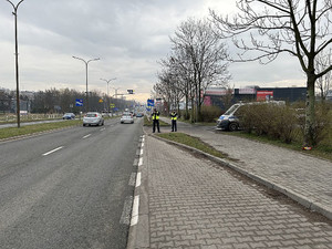 Na zdjęciu widać policjantów ruchu drogowego ubranych w kamizelki odblaskowe w trakcie działań NURD. Policjant dokonuje pomiaru prędkości w rejonie przejścia dla pieszych.