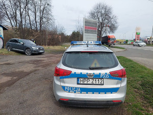 Na zdjęciu widać policyjny radiowóz oraz pojazd zatrzymany do kontroli, przy którym stoi umundurowany policjant ruchu drogowego.