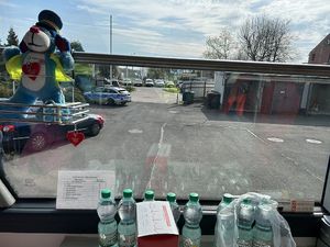 Na zdjęciu widać maskotkę Śląskiej Policji umieszczoną na oknie ambulansu krwiodawstwa, a w tle policyjny parking.