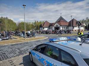 Na zdjęciu widać policyjny radiowóz, a w tle motocykle na przykościelnym parkingu.