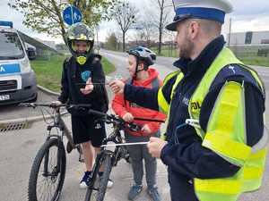 Na zdjęciu widać policjanta, który rozdaje odblaski dwóm nastolenim rowerzystom.