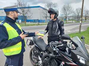 Na zdjęciu widać policjanta, który przekazuje odblaskową kamizelkę motocykliście.