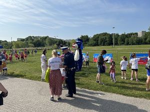 Na zdjęciu widać policjanta, Sznupka i przedszkolaków. Mundurowy rozdaje odblaski.