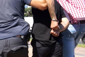 Na zdjęciu widać mężczyznę w kajdankach prowadzonego przez policjantów.