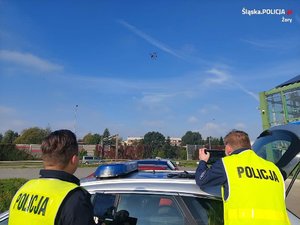 Na zdjęciu widać policjantów, radiowóz i policyjnego drona. W tle znajduje się DK81.