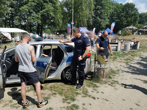 Na zdjęciu widać policjantów przed radiowozem, mężczyznę oraz dziewczynkę trzymającą policyjną tarczę.