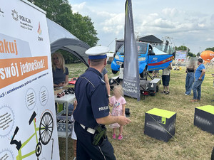 Na zdjęciu widać policjanta przy rollupie nawiązującym do akcji, a w tle stanowiska partnerów akcji.