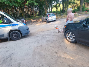 Na zdjęciu widać męzczyznę opartego o samochód, który trzyma na smyczy swojego psa. Obok stoi policyjny radiowóz.