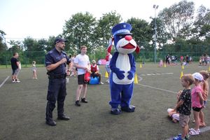 Na zdjęciu widać policjanta z mikrofonem w ręku, a obok Sznupka i dzieci.