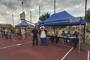 Na zdjęciu widać policjanta oraz maskotkę Śląskiej Policji podczas pikniku spoortowego w dzielnicy osiedle Gwarków.