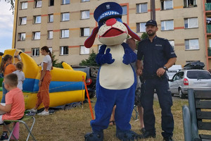Na zdjęciu widać policjanta oraz maskotkę Śląskiej Policji, w tle widać dmuchany zamek i dzieci.