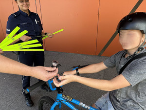 Na zdjęciu widać policjantów, którzy przekazują odblaskową listwę i dzwonek chłopcu na rowerze.