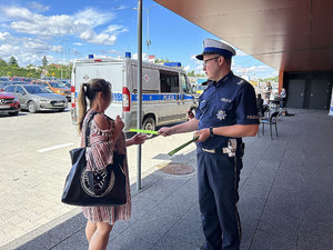 Na zdjęciu widać policjanta przekazującego kobiecie odblaskowy element.
