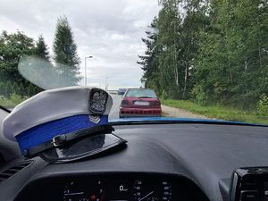 Na zdjęciu widać czapkę policyjną na podszybiu radiowozu, a przed pojazdem w tle widać bordowy samochód osobowy.