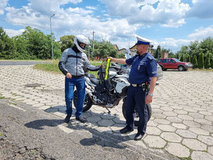 Na zdjęciu widać policjanta wręczającego odblaskową kamizelkę motocykliście.