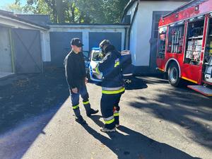 Na zdjęciu widać strażaka i mężczyznę, który przed zadaniem ubrać musiał strażacki kombinezon.