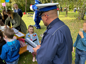 Na zdjęciu widać policjanta rozdającego odblaski dzieciom podczas pikniku.