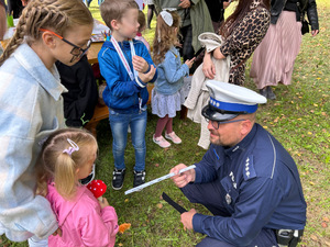 Na zdjęciu widać kucającego policjanta, który przekazuje odblask małej dziewczynce.