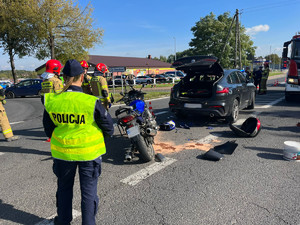 Na zdjęciu widać policjantkę w odblaskowej kamizelce na miejscu wypadku drogowego. Obok widać samochód bmw i motocykl honda.