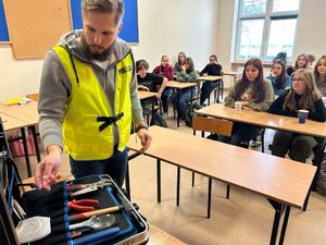 Na zdjęciu widać policjanta ubranego w odblaskową kamizelkę, policjant prezentuje walizkę technika kryminalistyki.