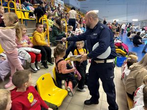 Na zdjęciu widać policjanta oraz Sznupka, w tle odbywające się rozgrywki.