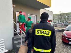 Na zdjęciu widać policjantkę, strażaka i elfy wchodzące do budynku.