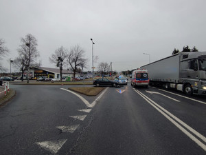 Na zdjęciu widać miejsce wypadku z udziałem rowerzysty i mercedesa. Obok widać samochód ciężarowy, radiowóz i karetkę pogotowia. W tle sklep wielobranżowy.