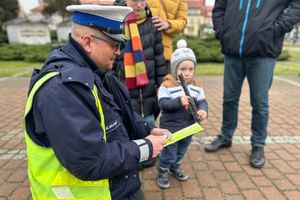 Na zdjęciu widać policjanta przekazującego odblaski. Obok widać chłopca z rodziną.