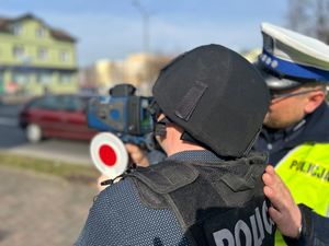 Na zdjęciu widać policjanta ruchu drogowego oraz mężczyznę, który trzyma w dłoni miernik prędkości.