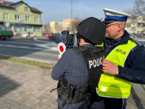 Na zdjęciu widać policjanta, który prezentuje mężczyźnie działanie policyjnego miernika prędkości.