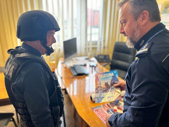 Na zdjęciu widać komendanta żorskiej Policji w trakcie rozmowy z mężczyzną, Komendant trzyma w dłoni policyjną gazetę.