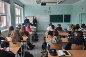 Na zdjęciu widać policjantów i uczniów w trakcie zajęć w szkolnej klasie.