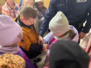 Na zdjęciu widać policjanta, który prezentuje dzieciom jak używa się kajdanek.