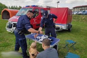 Na zdjęciu widać policjantów przy stoisku promocyjnym, w tle pojazdy strażackie.