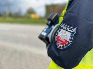 Na zdjęciu widać policjanta ruchu drogowego stojącego przy drodze z laserowym miernikiem prędkości.