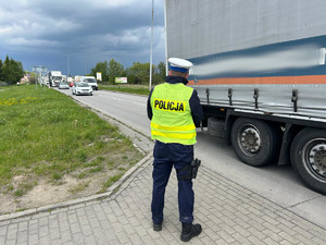 Na zdjęciu widać policjanta stojącego przy jezdni i dokonującego pomiaru prędkości pojazdów.