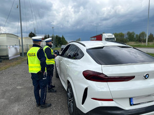 Na zdjęciu widać policjantów stojących przy kontrolowanym, białym samochodzie.