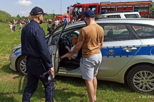 Na zdjęciu widać policjanta przed radiowozem oraz uczestników festynu. Chłopiec siedzi &quot;za kierownicą&quot; w zaparkowanym pojeździe.