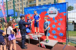 Na zdjęciu widać policjanta wręczającego nagrody osobom na podium.