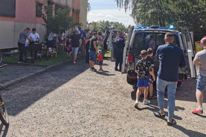 Na zdjęciu widać policyjny radiowóz, policjanta oraz uczestników festynu.